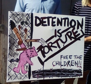 'Detention is torture', large colourful sign, held by its two makers, 2015.
